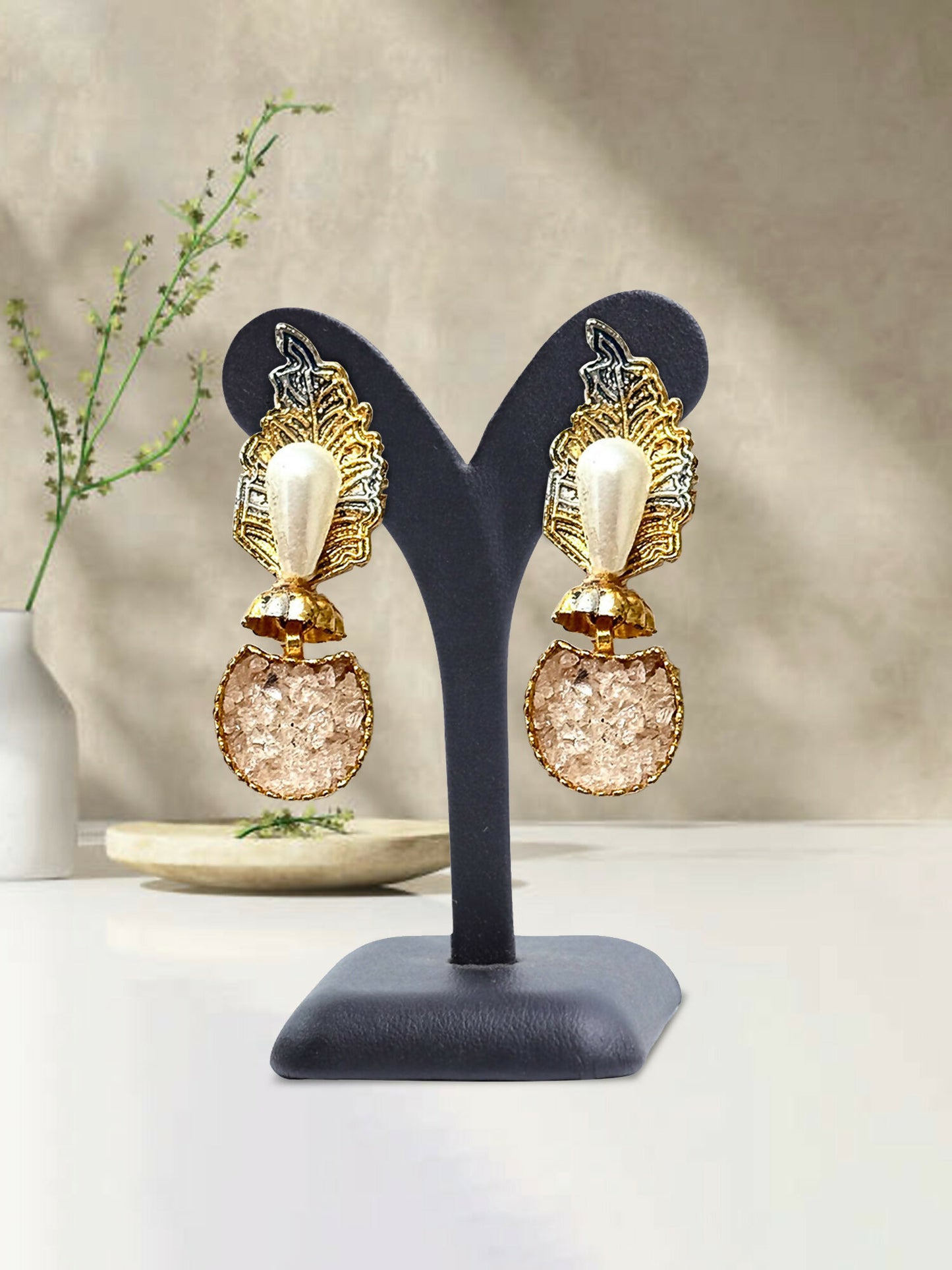 Glitter Jewellery gold-toned statement earrings featuring pearl accents, leaf motifs, and textured round drops, displayed on a black stand.