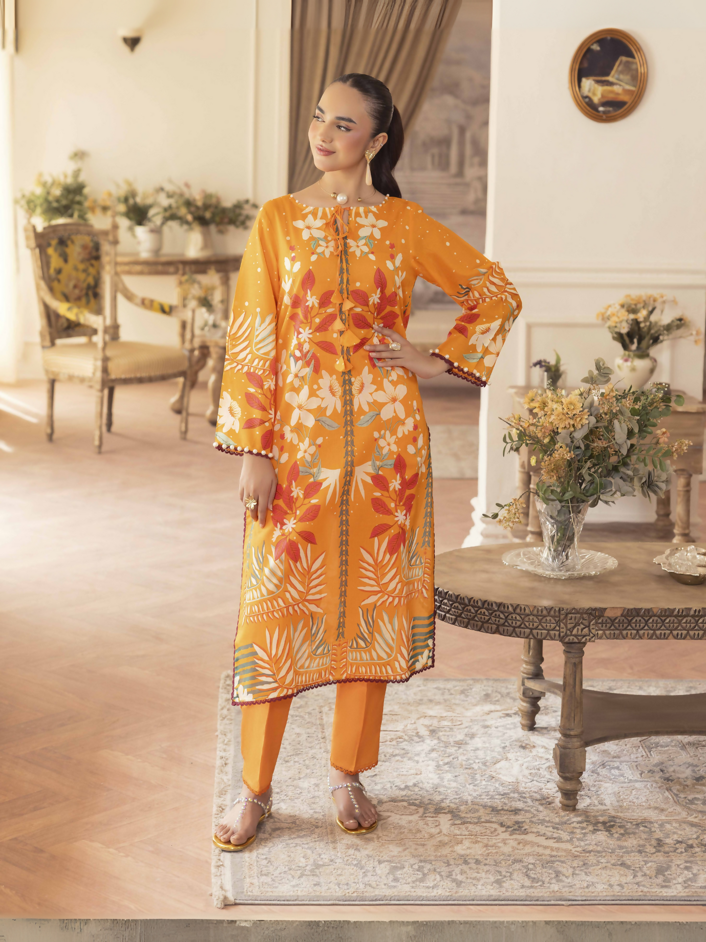 Woman wearing an orange 2 piece unstitched lawn suit with colorful floral print and dyed cotton trouser.