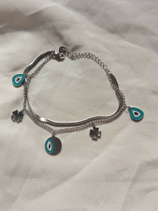 Joyels layered silver bracelet featuring evil eyes for protection and clovers for luck, blending symbolism with style.