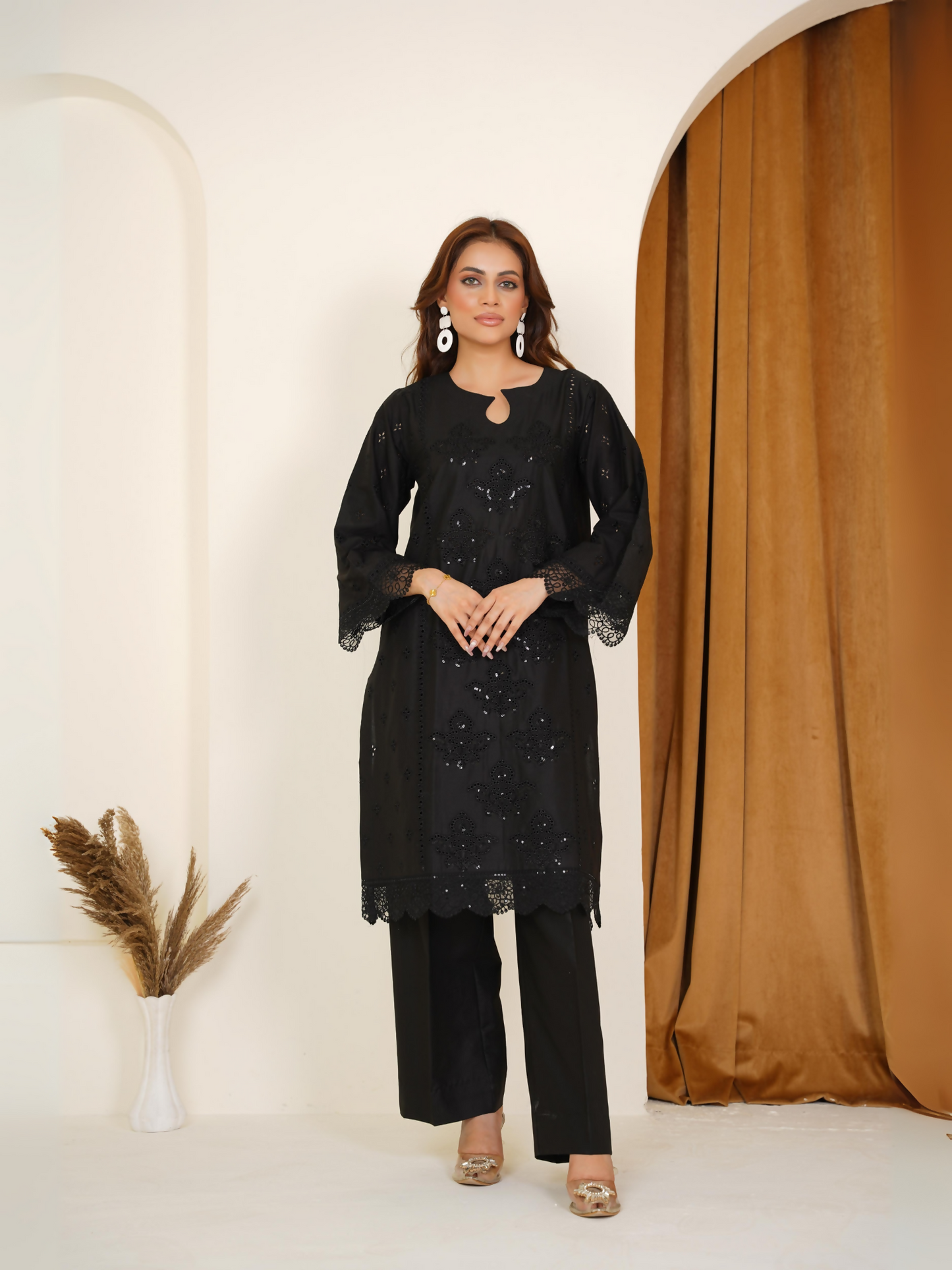 Woman wearing a black 2-piece suit with black-on-black embroidery and lace-trimmed sleeves, paired with a plain black trouser.