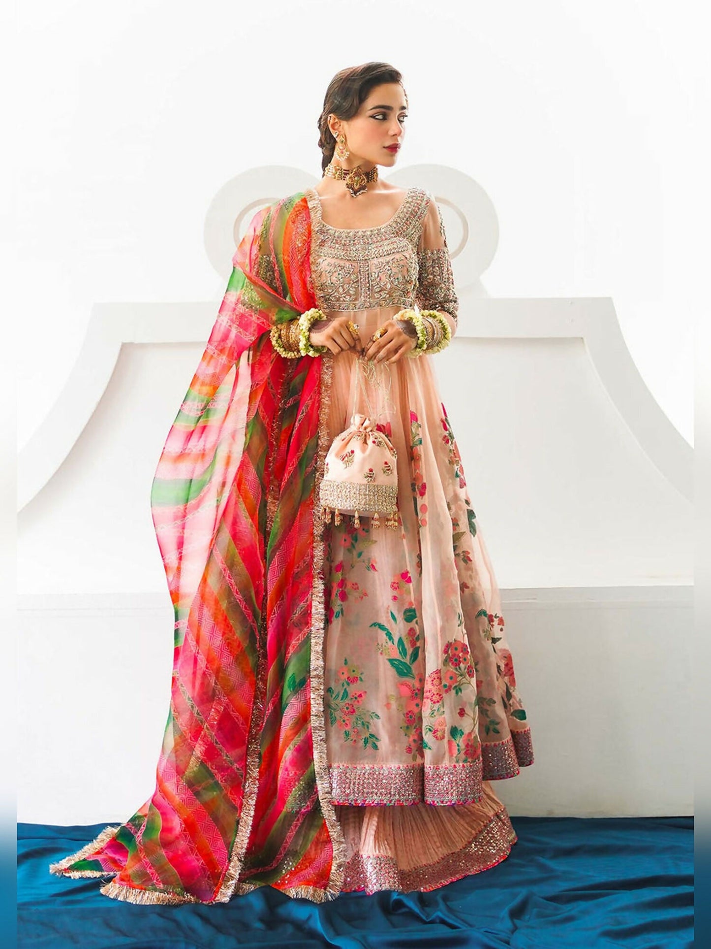 Stitched 3-piece suit by Hussain Rehar with rose gold organza peshwaz featuring embellishments and printed panels, paired with crushed silk sharara and multicolored striped organza dupatta with kiran.