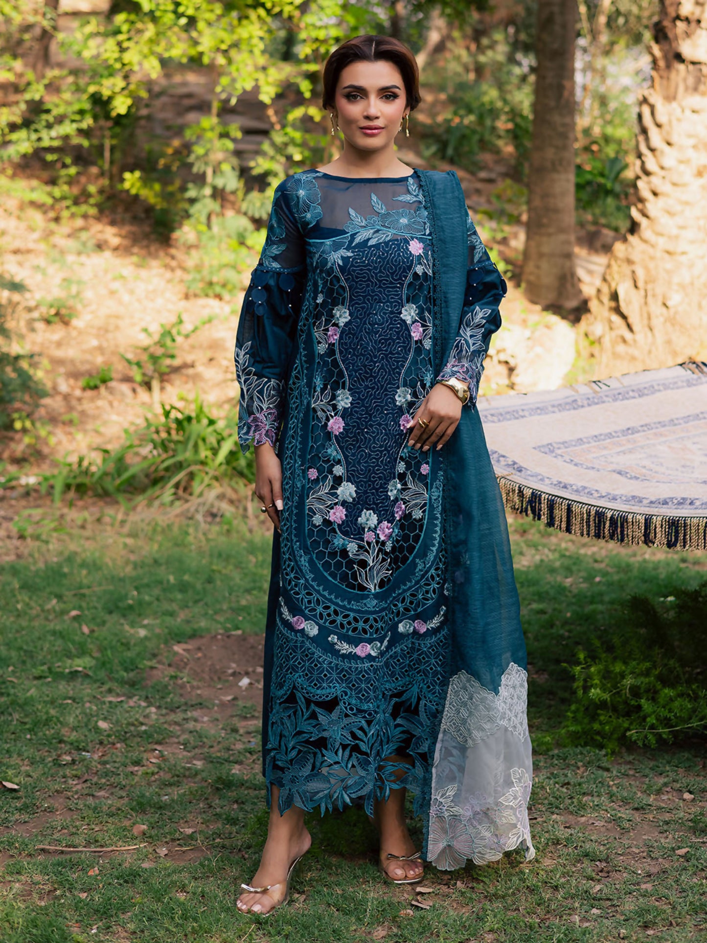 Girl standing wearing an unstitched 3-piece suit with embroidered lawn shirt featuring center organza panel, embroidered sleeves, neckline, and daman, paired with an embroidered Monark dupatta and dyed Cambridge trouser with slip, perfect for formal occasions.