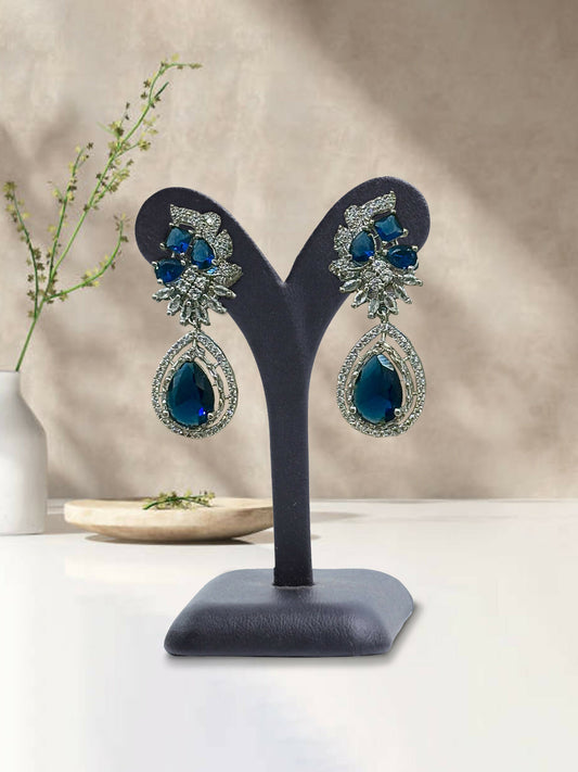 Glitter Jewellery Silver-toned drop earrings with blue crystals and intricate detailing on display stand.