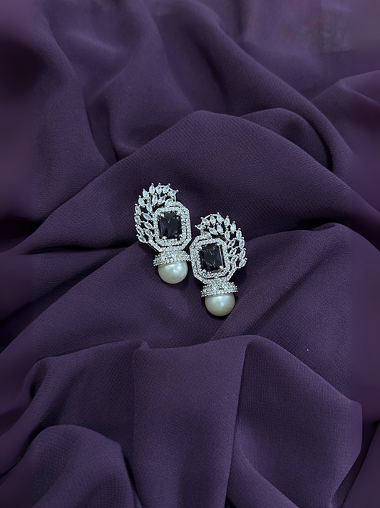 Black crystal and pearl drop earrings with silver-toned setting and clear crystal accents, displayed on a deep purple fabric background