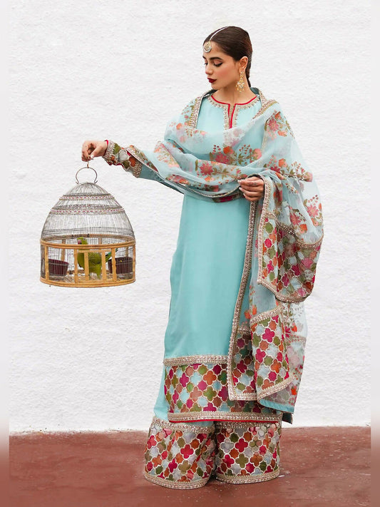 Hussain Rehar stitched 3-piece suit featuring an ice blue raw silk embellished shirt, raw silk palazzo pants with detailed border, and organza dupatta with block-printed motifs and multi-colored border.