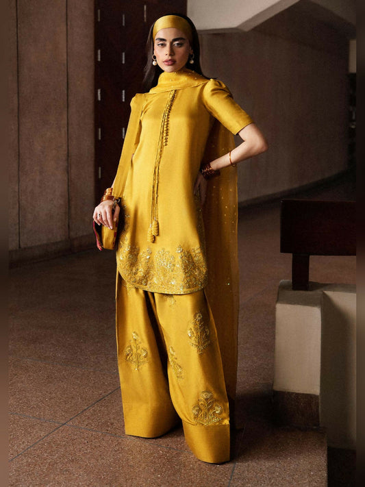 Stitched 3-piece suit by Hussain Rehar with mustard short raw silk shirt featuring puff sleeves and precious stone embellishments, paired with embellished shalwar and organza dupatta with sequin spray and satin silk pallu.