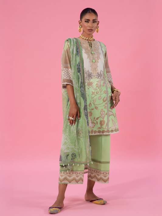 Woman wearing a green unstitched 3-piece suit featuring golden printed lawn shirt, matching printed dupatta, and dyed cambric trouser
