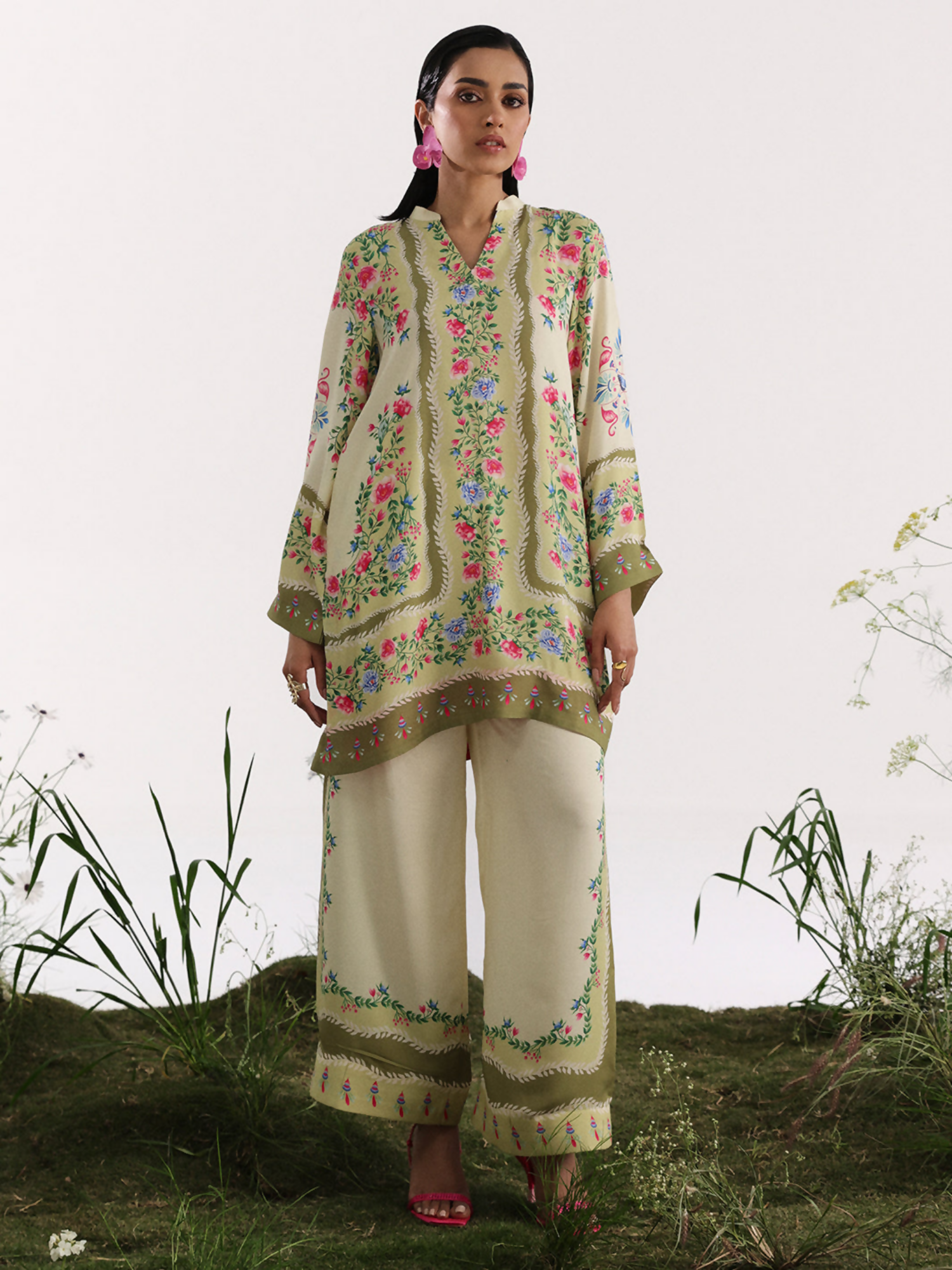 Model wearing a cream and olive silk co-ord set featuring multicolor floral patterns and traditional border designs.