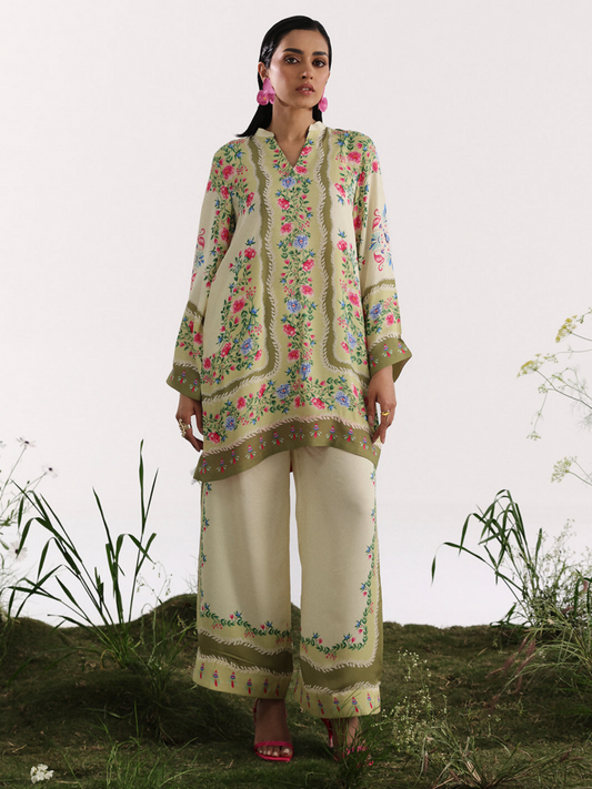 Model wearing a cream and olive silk co-ord set featuring multicolor floral patterns and traditional border designs.