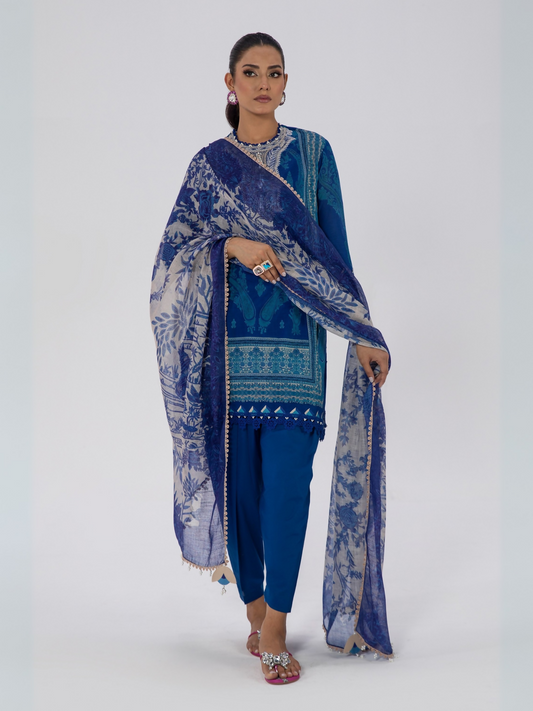 Woman wearing a blue unstitched 3-piece Sana Safinaz lawn suit with printed shirt, printed dupatta, and dyed trouser.