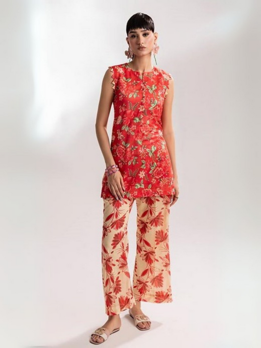 Woman wearing a sleeveless red floral printed lawn shirt paired with cream trousers featuring red floral patterns, standing with one hand in pocket against a plain background.