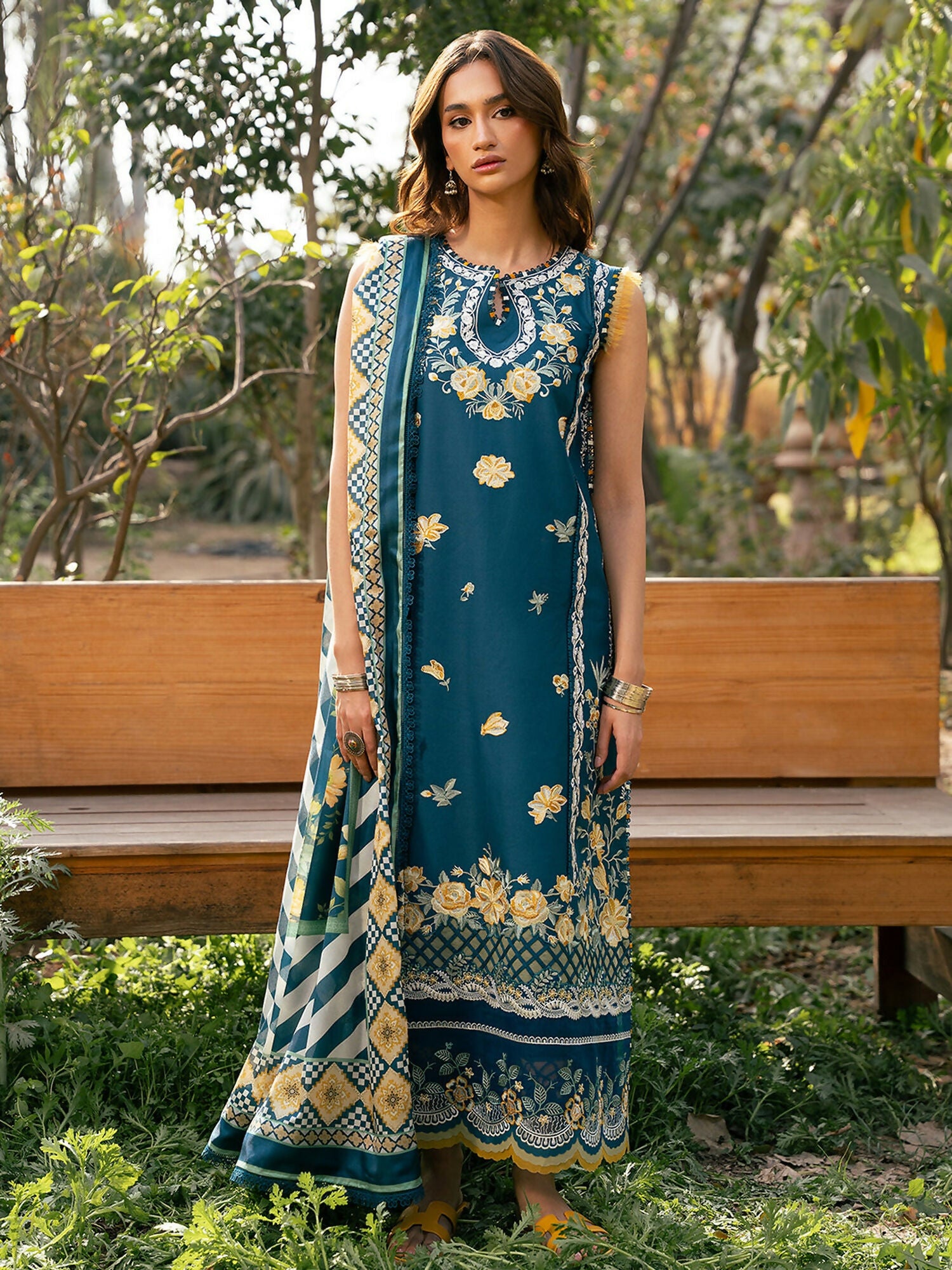 Unstitched teal embroidered lawn outfit with mustard floral motifs, lace detailing, printed silk dupatta, and dyed cotton trouser.