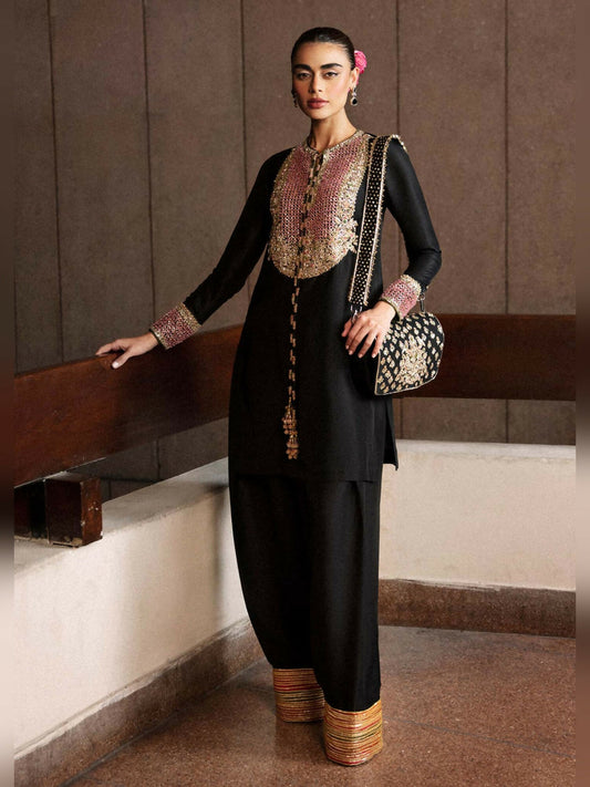 Stitched 3-piece suit by Hussain Rehar with black raw silk short shirt featuring embellished neckline and tassels, paired with shalwar with colorful gota border and organza dupatta with sequin spray.
