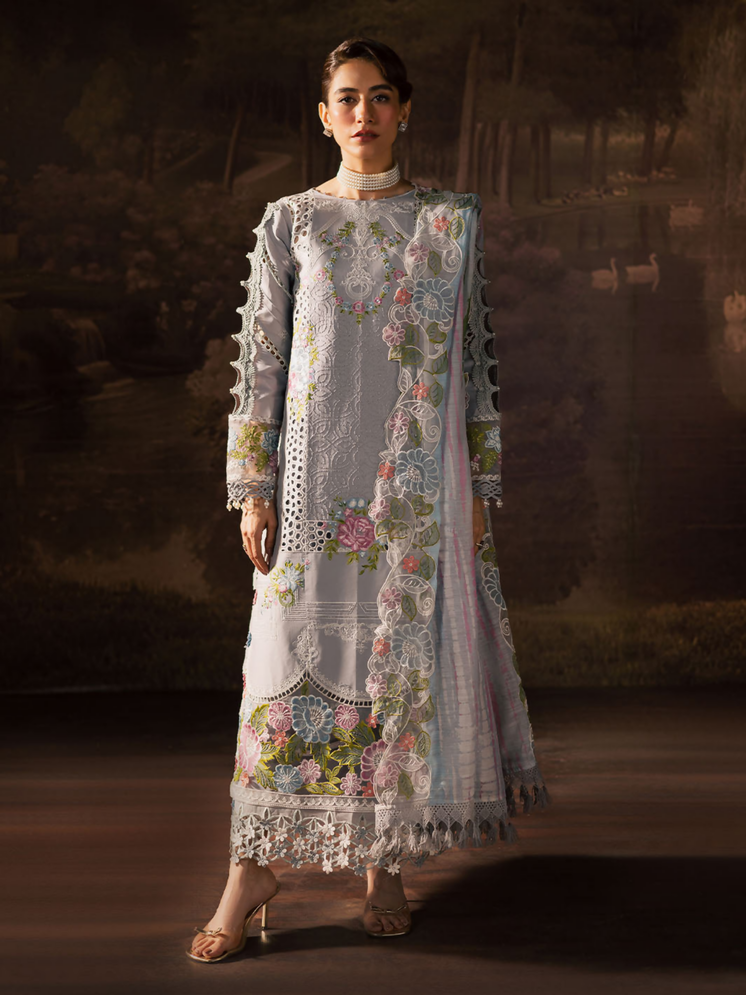 Girl standing wearing an unstitched 3-piece suit with embroidered lawn shirt front, daman, and sleeves, styled with a printed embroidery Monark dupatta and dyed Cambridge trouser with slip, ideal for graceful festive wear.