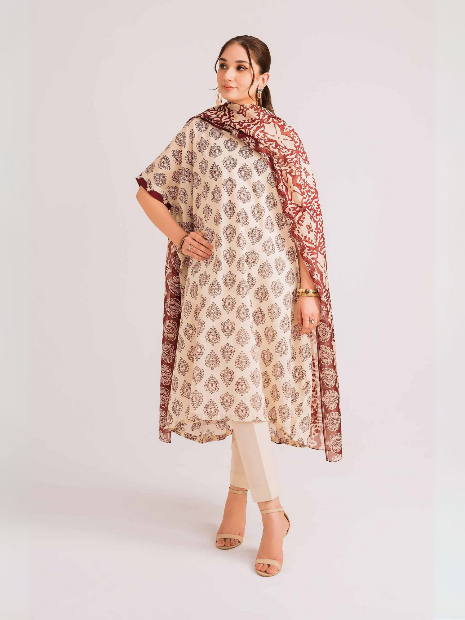 Nishat unstitched 3-piece lawn suit with ethnic print shirt, maroon voile dupatta, and cambric trouser in off-white.