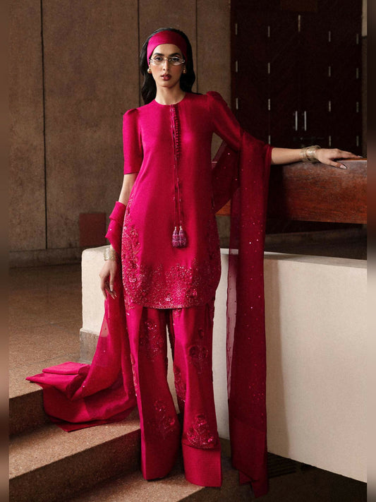 Stitched 3-piece suit by Hussain Rehar featuring a hot pink short raw silk shirt with puff sleeves, embellished detailing, and precious stones, paired with an embellished raw silk shalwar, and an organza dupatta with heavy sequin spray and satin silk pallu.