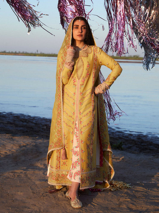 Mustard-yellow embroidered lawn tunic with floral and geometric patterns, ivory printed cotton trousers with red and green floral design, and mustard-yellow organza dupatta with embroidered motifs, lace, and tassel details.