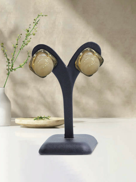 Glitter Jewellery glossy beige stud earrings with a rounded dome design and metallic trim displayed on an earring stand.