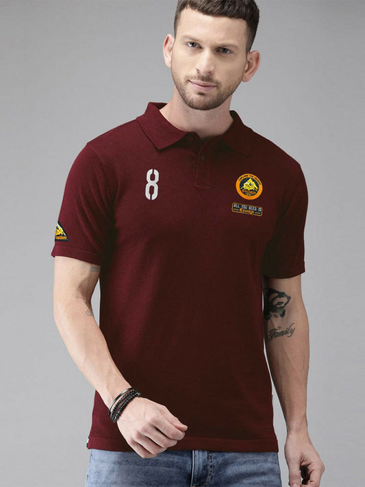 A man wearing a maroon polo shirt with embroidered logos on the chest and sleeve, styled with a classic knit collar and button placket.