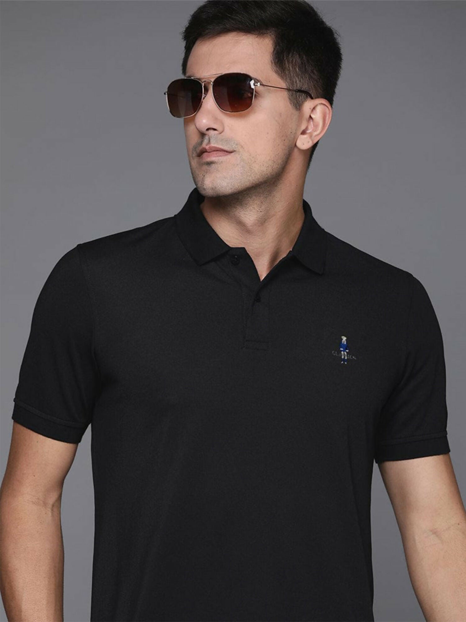A man wearing a black cotton polo shirt with a classic knit collar, front button placket, and a fine embroidered logo on the left chest.