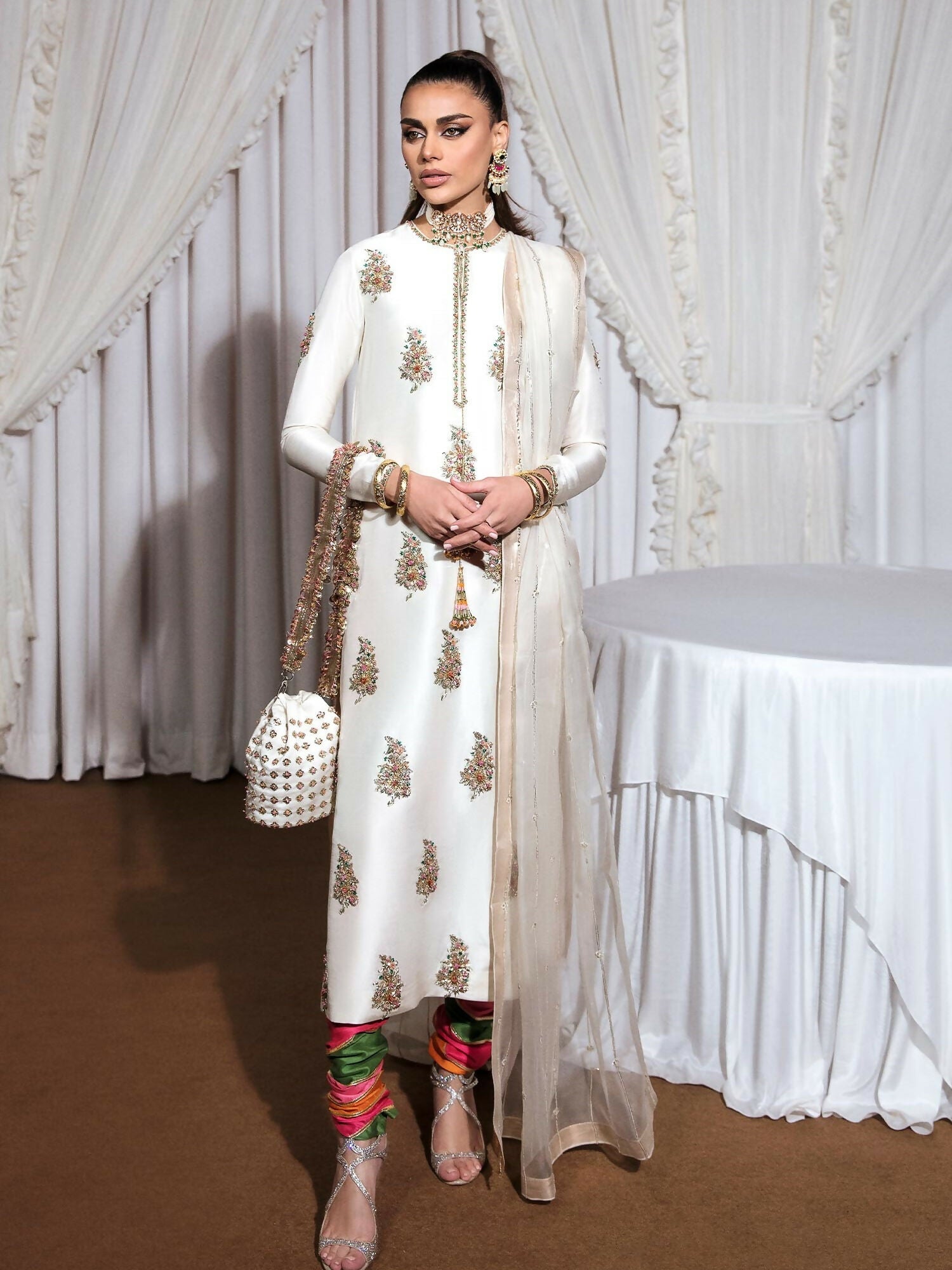 Ivory raw silk stitched 3-piece suit Blanc by HussainRehar featuring an embellished neckline with gold nakshi, sequins, pink crystals, and multicolor bugle beads with tassel details, paired with a multi-colored printed satin chooridar with gotta work and an organza dupatta with multi-head detailing and lappa on all four borders, ideal for festive occasions.