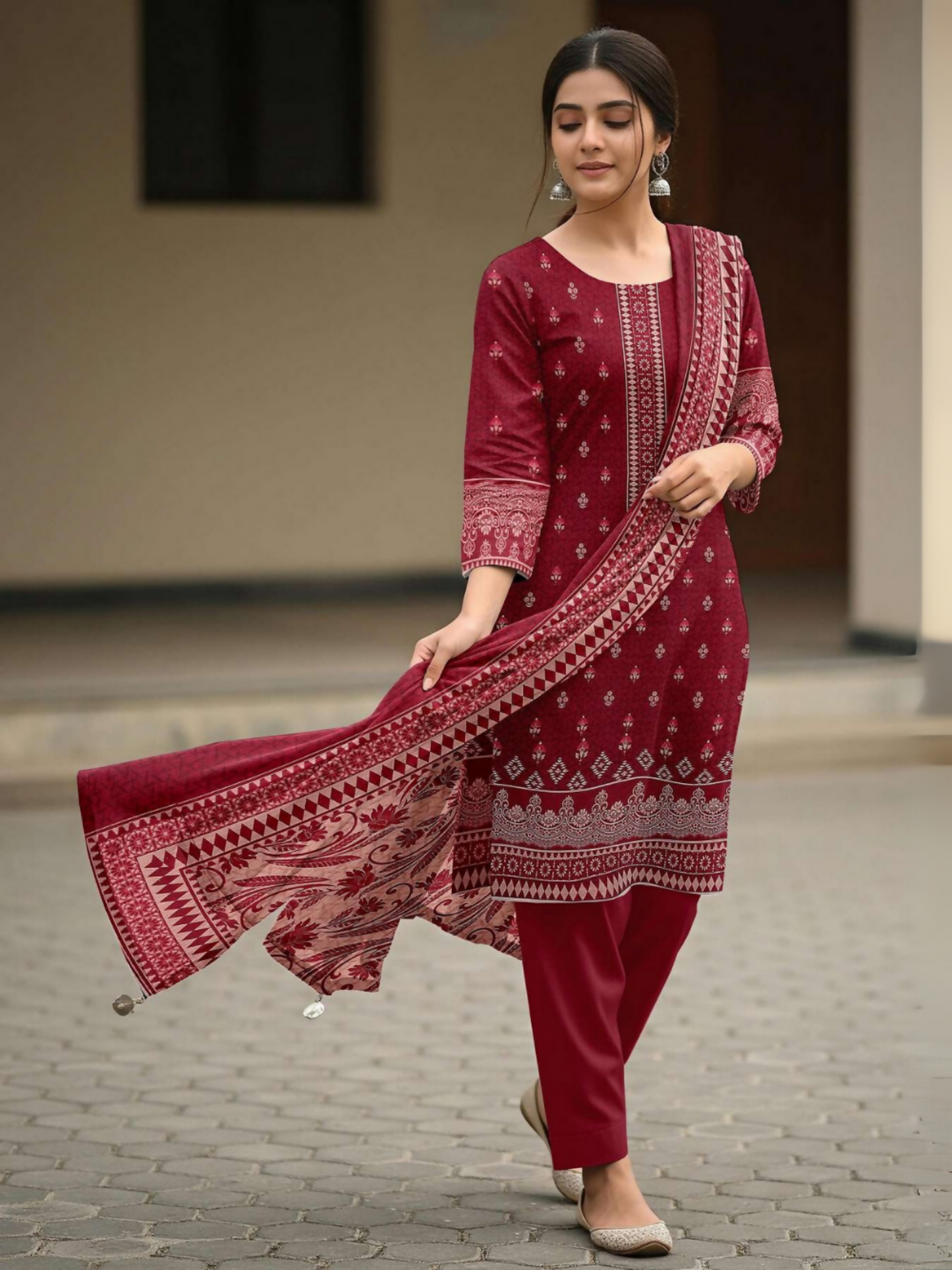 Woman standing in an unstitched 3-piece maroon red suit featuring a digital printed lawn shirt with traditional patterns, matching printed voile dupatta, and plain dyed cotton trouser.