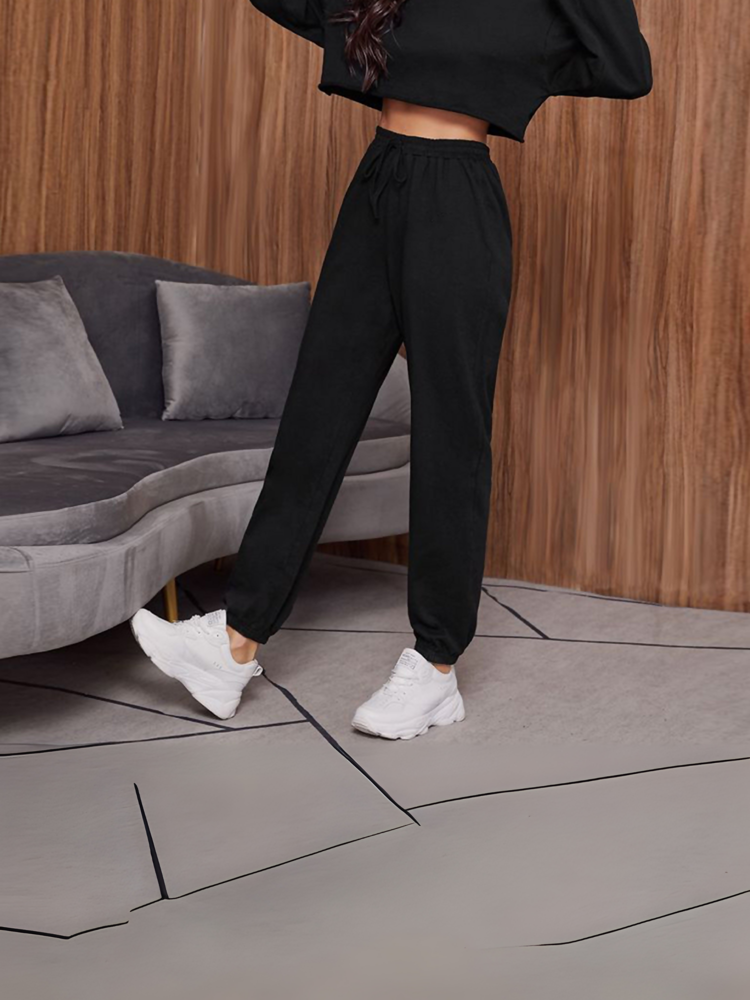 Women's black fleece trouser with drawstring waist and elasticated cuffs, styled with white sneakers in a cozy indoor setting.
