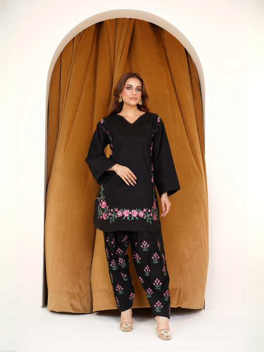 Woman wearing a stitched black 2-piece suit from the Karam Collection with delicate pink floral embroidery on shirt and trouser.