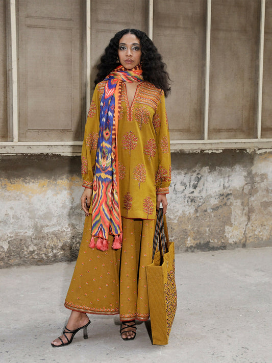 Woman wearing mustard karandi embroidered shirt with lace details and high-waisted karandi skirt with multi-color floral embroidery, 2-piece stitched suit.
