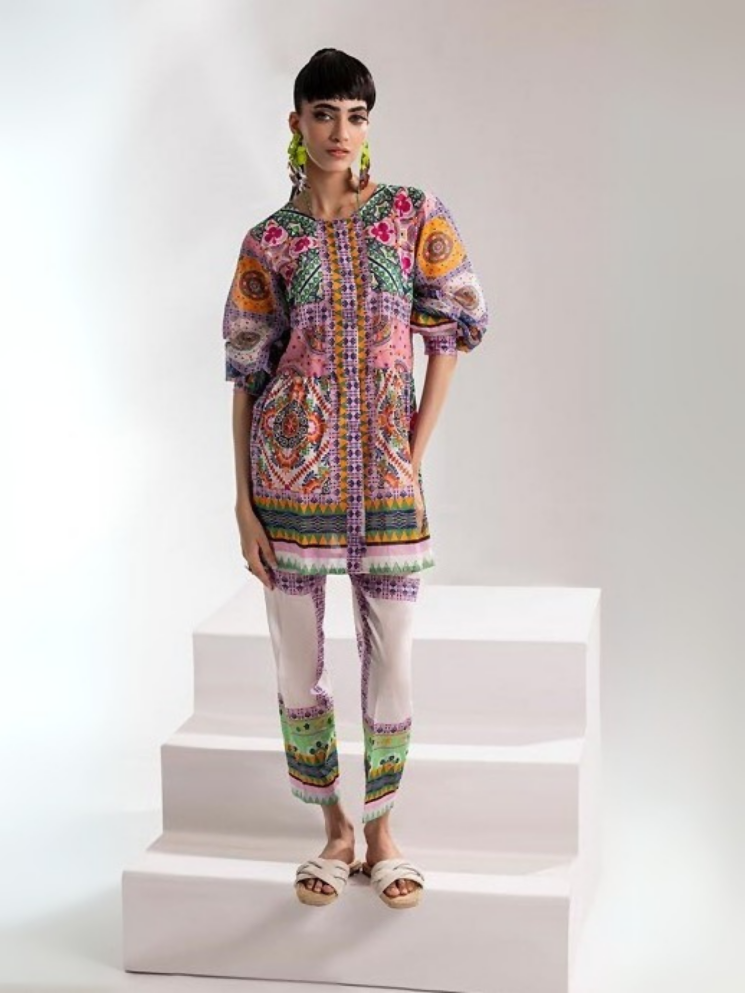 Woman wearing a vibrant mosaic-printed shirt in bold shades of orange, pink, green, and purple, paired with a matching printed trouser from Parizad's unstitched lawn collection.