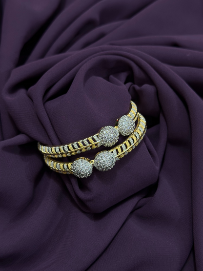 Close-up of two individual two-toned karas featuring pavé-textured spheres, crystal detailing, and black enamel accents – statement pieces from Glitter Jewellery.