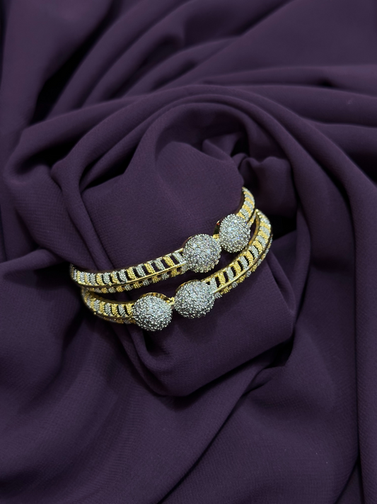 Close-up of two individual two-toned karas featuring pavé-textured spheres, crystal detailing, and black enamel accents – statement pieces from Glitter Jewellery.