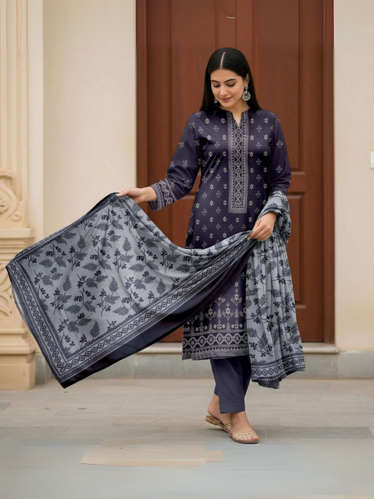 A woman in a navy blue printed suit with a silver-grey floral dupatta, standing gracefully in front of a wooden door.